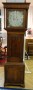 Englische Standuhr, um 1840, Eiche. Rechteckiges Unterteil, übergeordnetes Mittelteil mit einer Tür hinter der sich das Pendel befindet. Quadratisches Kopfteil, flankiert von Vollsäulen. Ziffernblatt mit arabischen Zahlen. Zentrale Datumsanzeige und Sekundenanzeige. Zwei Gewichte vorhanden. Ein identisches Exemplar steht im Weißen Haus.