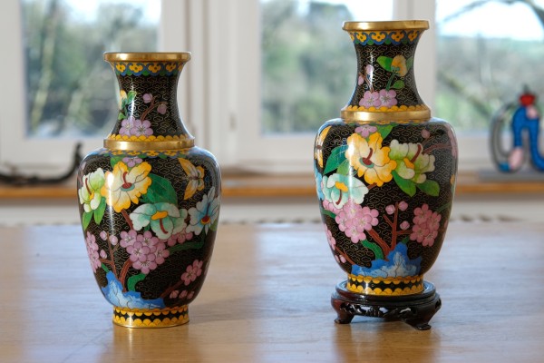 Japanische Cloisonné-Vasen. Schwarzer Grund, mit Prunusblüte und Wildrose verziert. Im Inneren vergoldet, sowie mit feiner Goldlinierung auf Emaille. Eine Vase mit Sockel. Eine der Vasen an der Öffnung bestoßen.